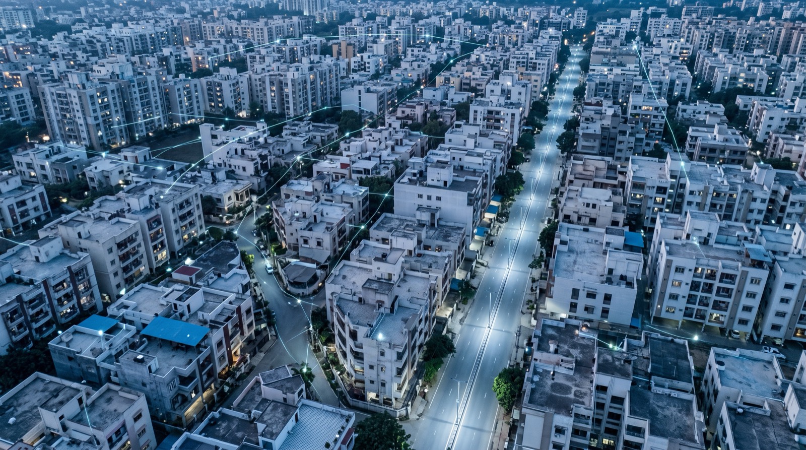 Aerial view of an Indian city neighbourhood at blue hour, its streets and windows lit